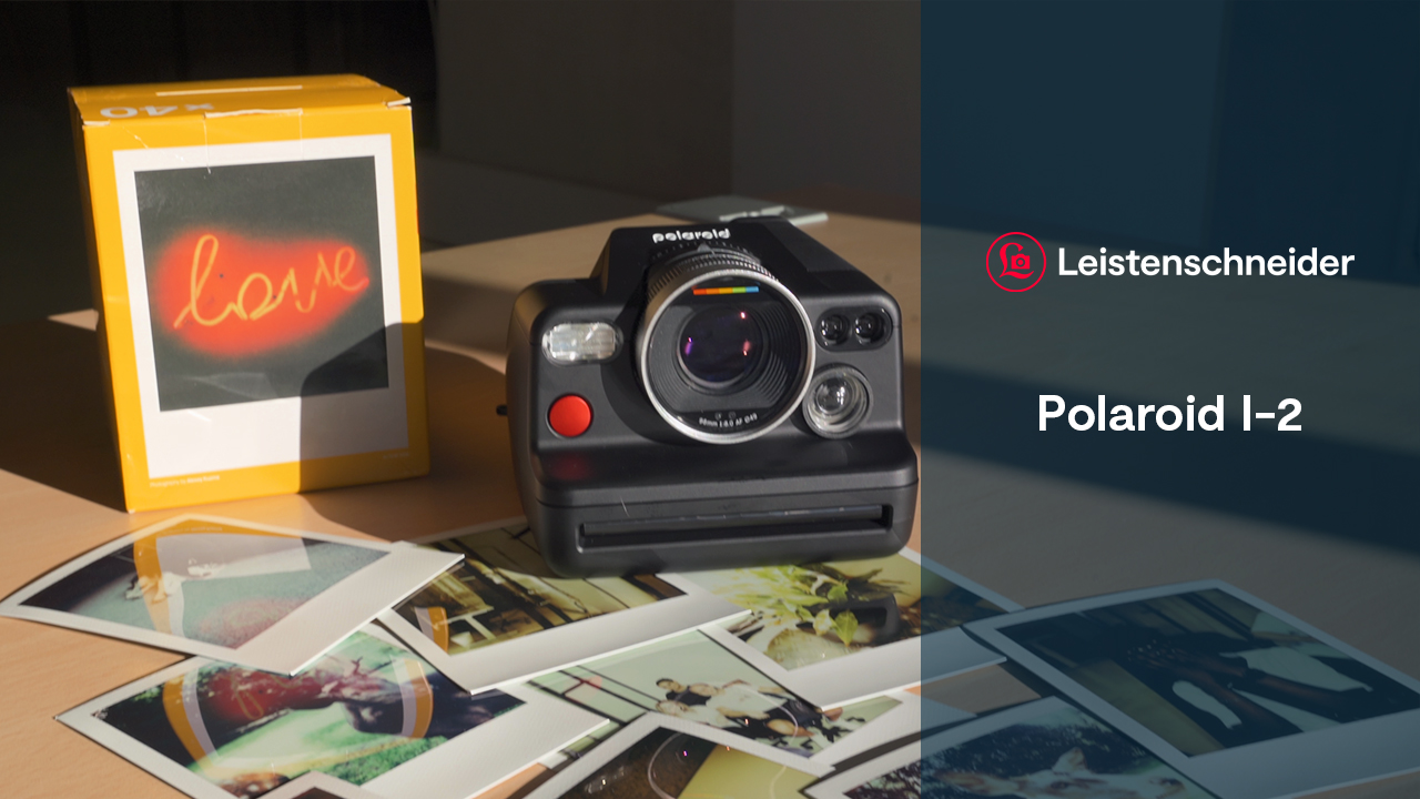 Die Polaroid I-2 mit vielen Fotos und einer Packung Filmen auf einem Tisch auf einem Banner steht "Leistenschneider - Polaroid I-2"